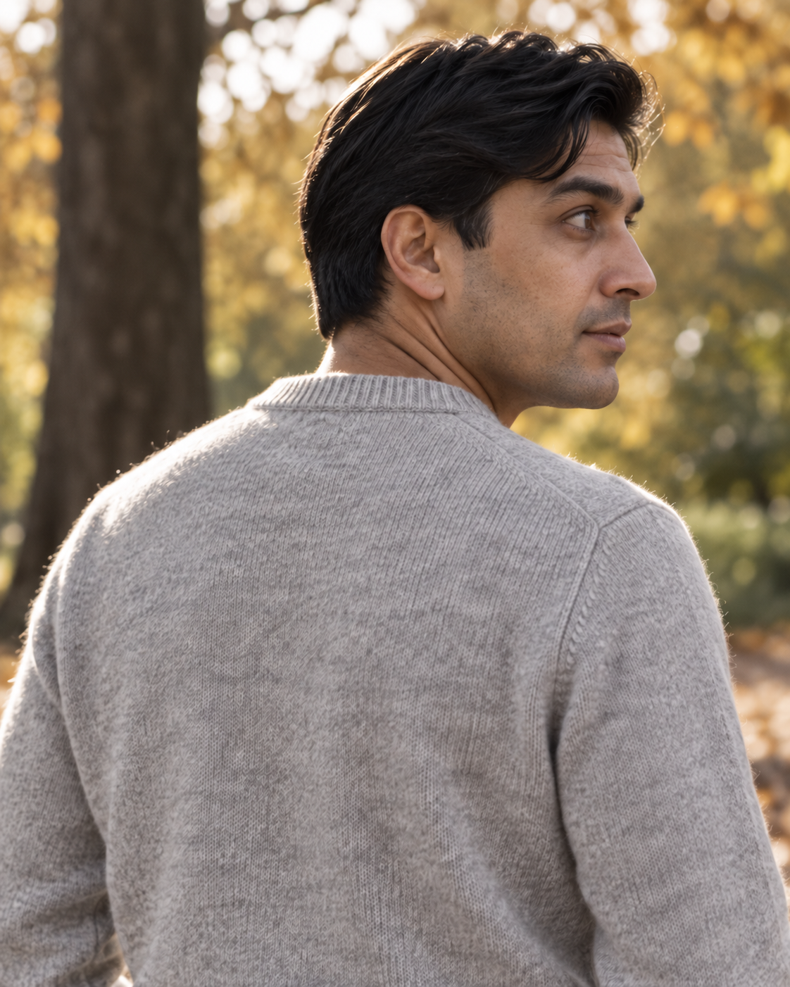 Man wearing the light grey Crewneck Sweater Soft Heritage, back view looking over his shoulder in a park