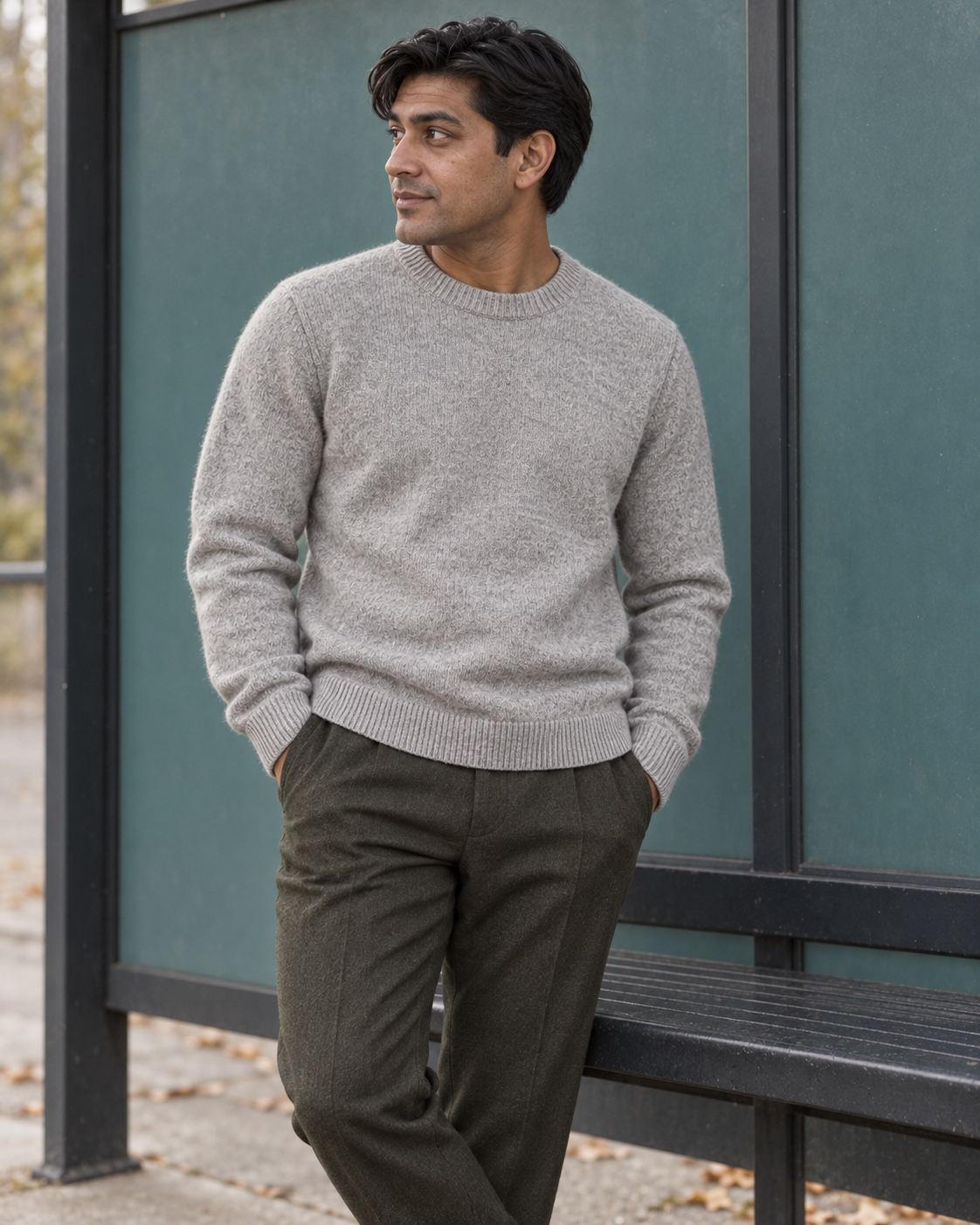 Man wearing the light grey Crewneck Sweater Soft Heritage with hands in trouser pockets at a bus shelter
