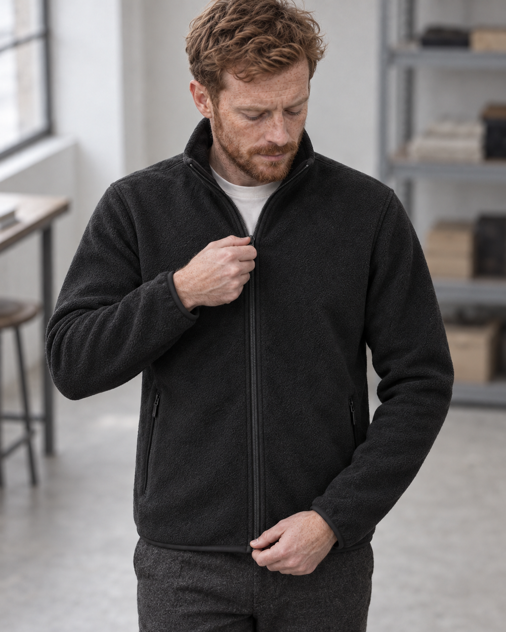 Man adjusting the zip of the charcoal Fleece Jacket Alpine Refined, viewed from above in a grey studio