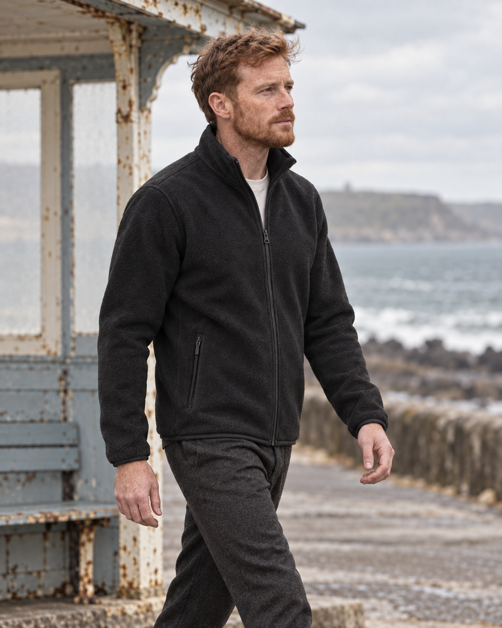 Man wearing the charcoal Fleece Jacket Alpine Refined in side view at a coastal shelter