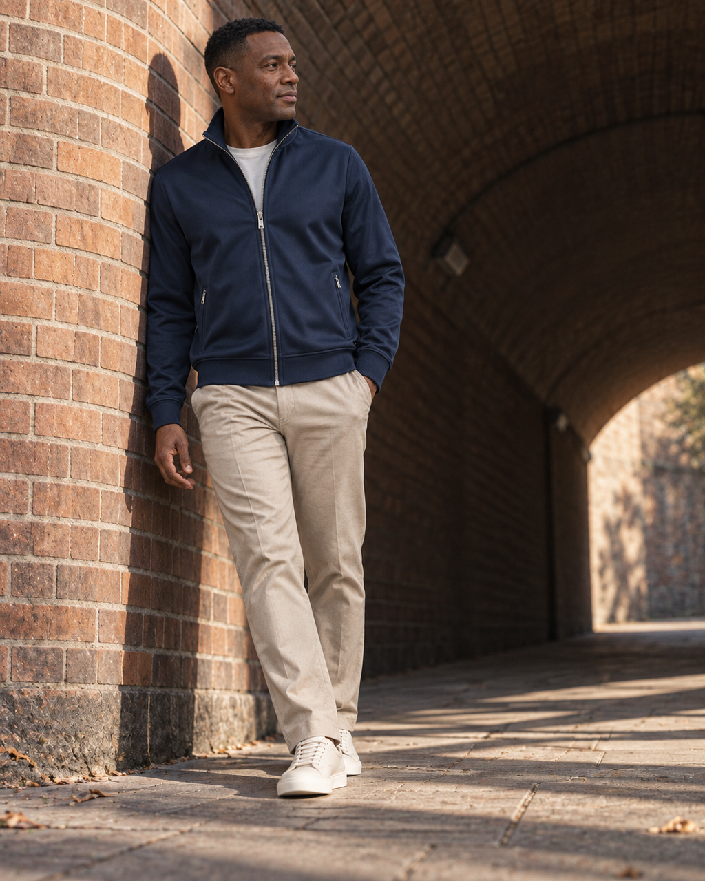 Full-length low-angle view of a man wearing the navy Track Jacket Heritage Signature in a brick passage